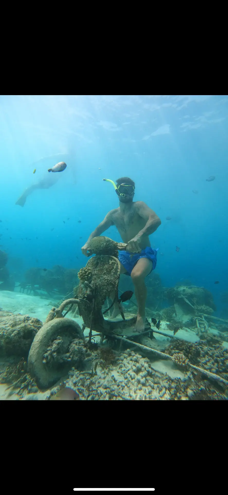 Snorkeler riding a rusted underwater scooter art installation